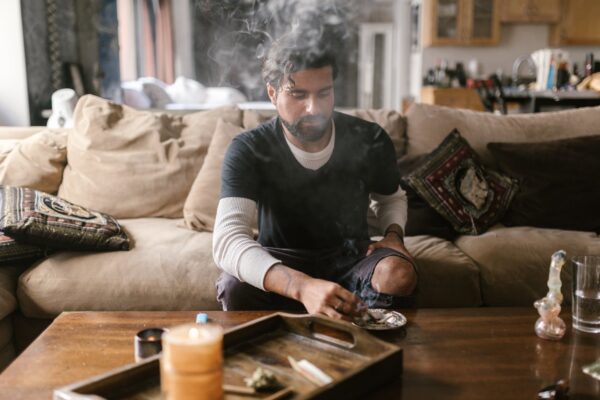 man in black and white long sleeve shirt sitting on couch smoking marijuana